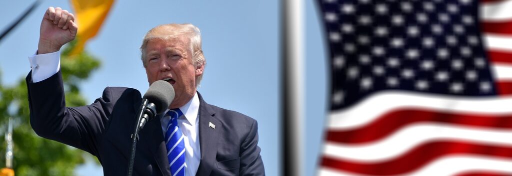 Donald Trump speaking beside an American flag, used in the context of 2025 U.S. trade tariffs